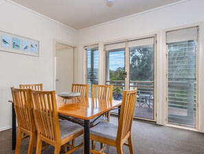 A dining area with a wooden table and chairs, a potted plant, and a view through large glass doors.