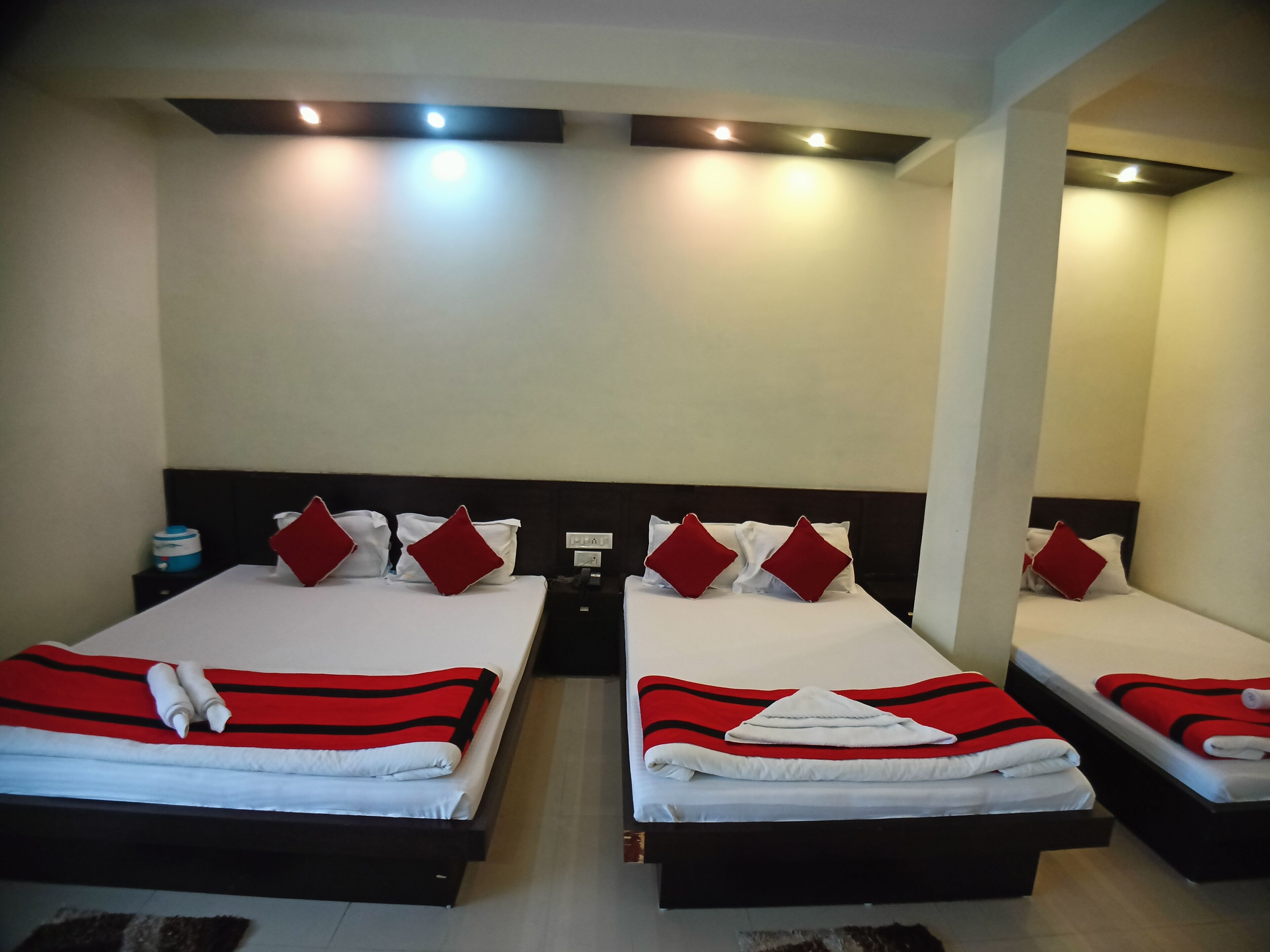 A hotel room with two beds, each with a red and white striped blanket, white pillows, and red accent pillows. There are bedside tables with lamps and a water dispenser.