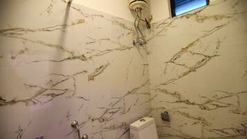 A bathroom with a marble wall, a handheld showerhead, a built-in toilet, and a window with blinds.