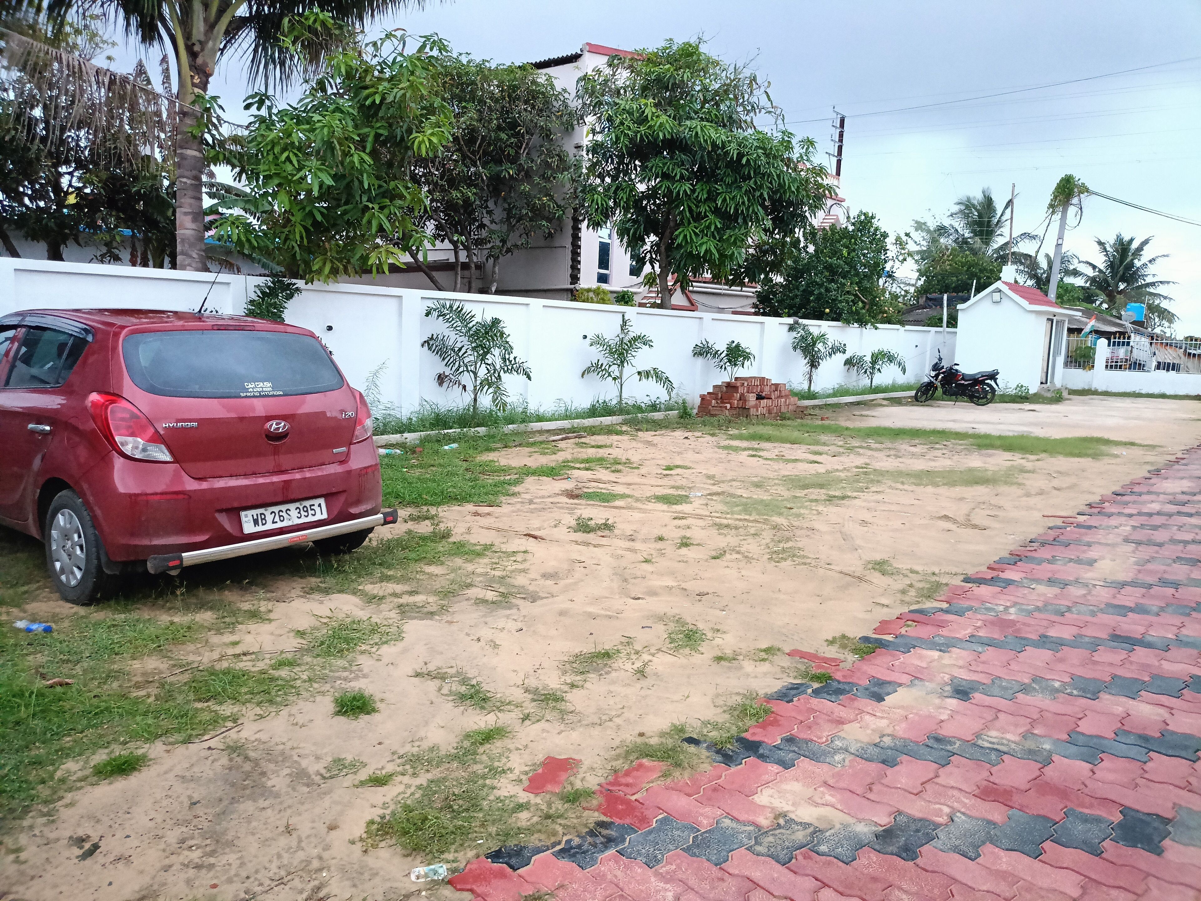 Un Hyundai I20 rojo estacionado en un terreno de tierra con un sendero pavimentado.