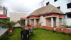 A courtyard with a thatched-roof building, a paved walkway, and a small garden area with chairs and potted plants. - Shinjini Resort (Kanthi)