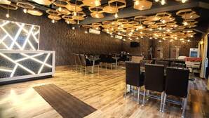 A modern restaurant interior with hexagonal ceiling lights, a geometric wall design, and a wooden floor. - Shinjini Resort (Kanthi)