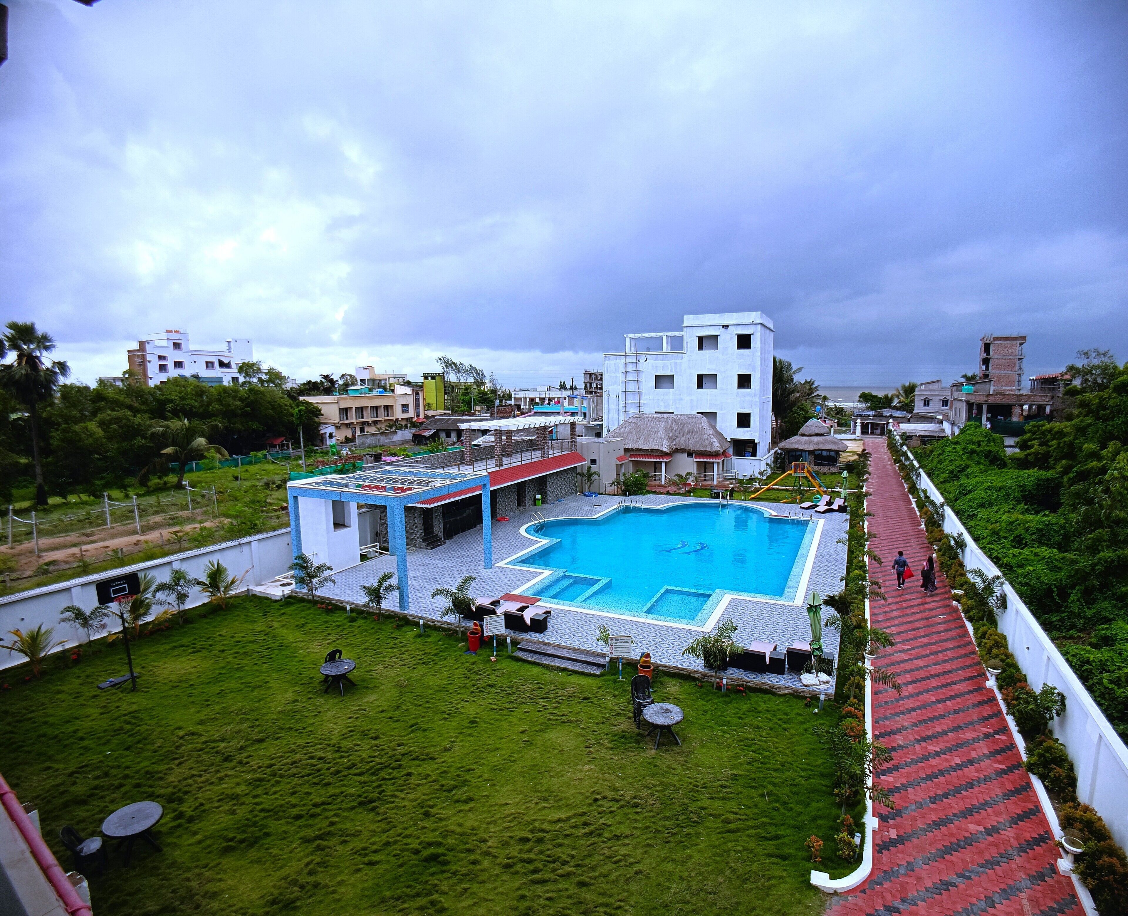 A swimming pool with a tiled deck, surrounded by a grassy area and a red brick pathway.