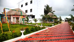 A pathway leading to a building with a thatched-roof structure, a playground, and a well-maintained garden. - Shinjini Resort (Kanthi)