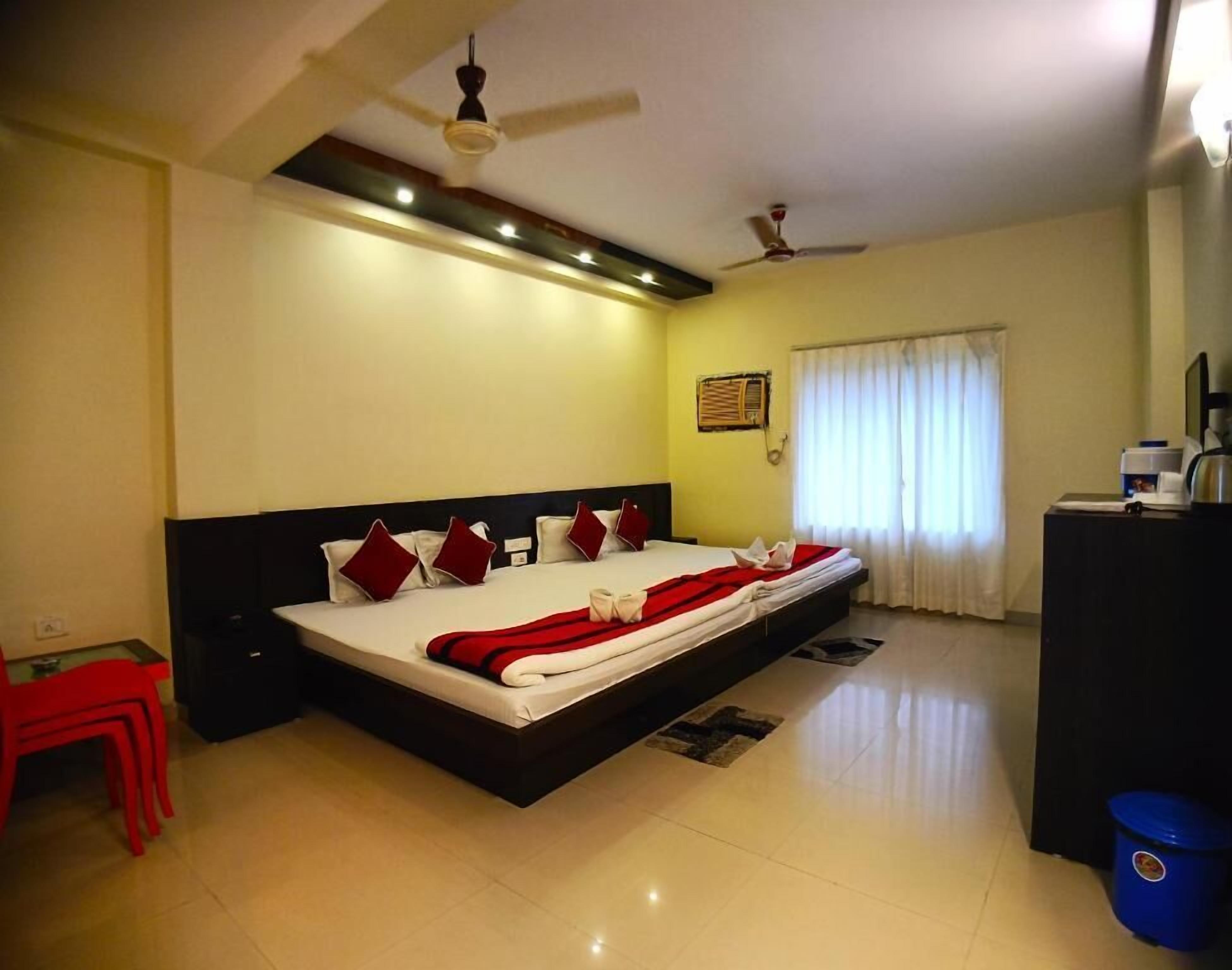 A bedroom with a large bed, two ceiling fans, a desk, and a window with curtains.