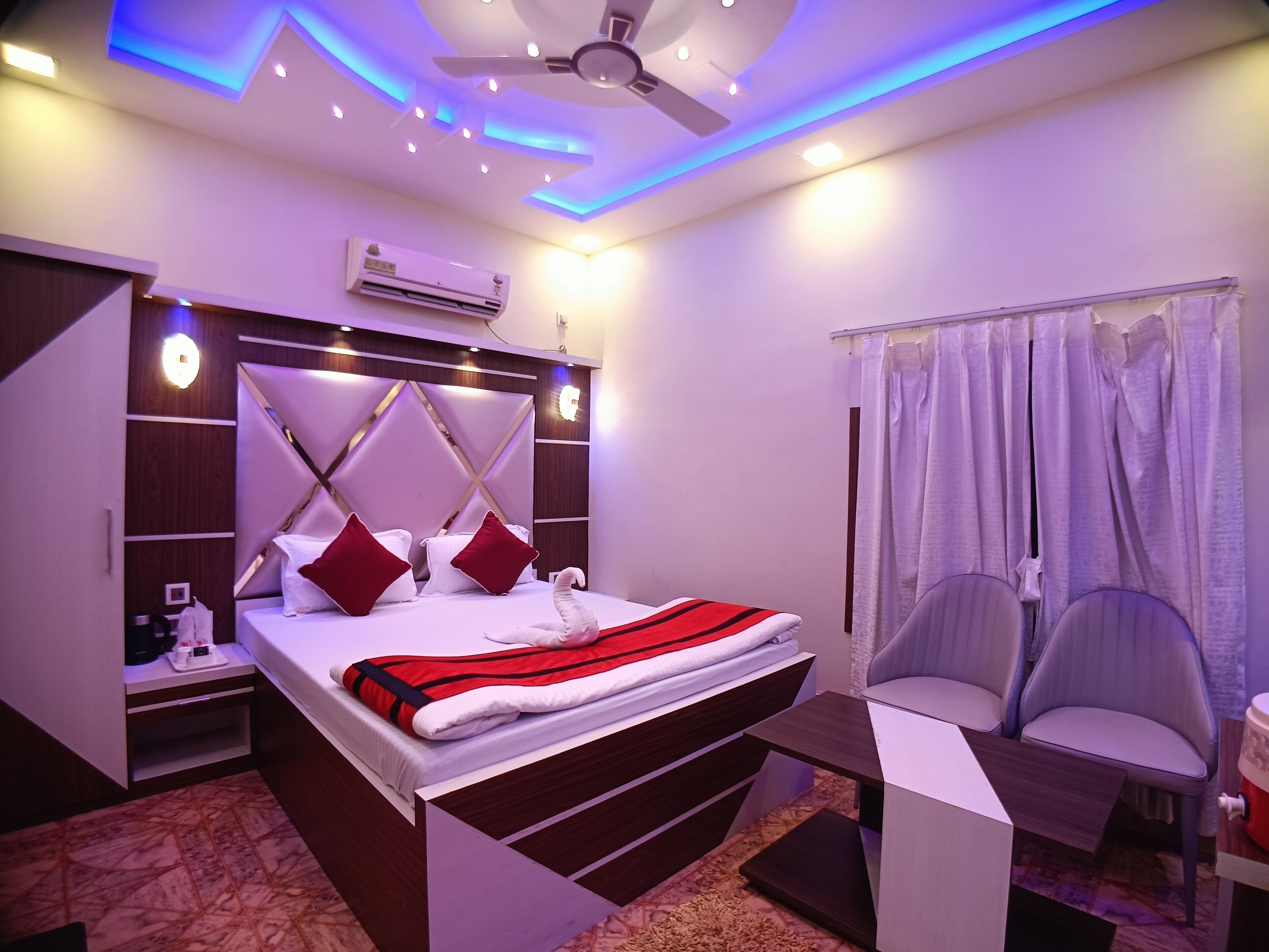 Une chambre moderne comprenant un lit, des tables de chevet, un ventilateur de plafond, un appareil de climatisation et un coin salon agrémenté de rideaux.