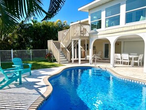 A swimming pool with a wooden deck, outdoor chairs, and a covered patio area.