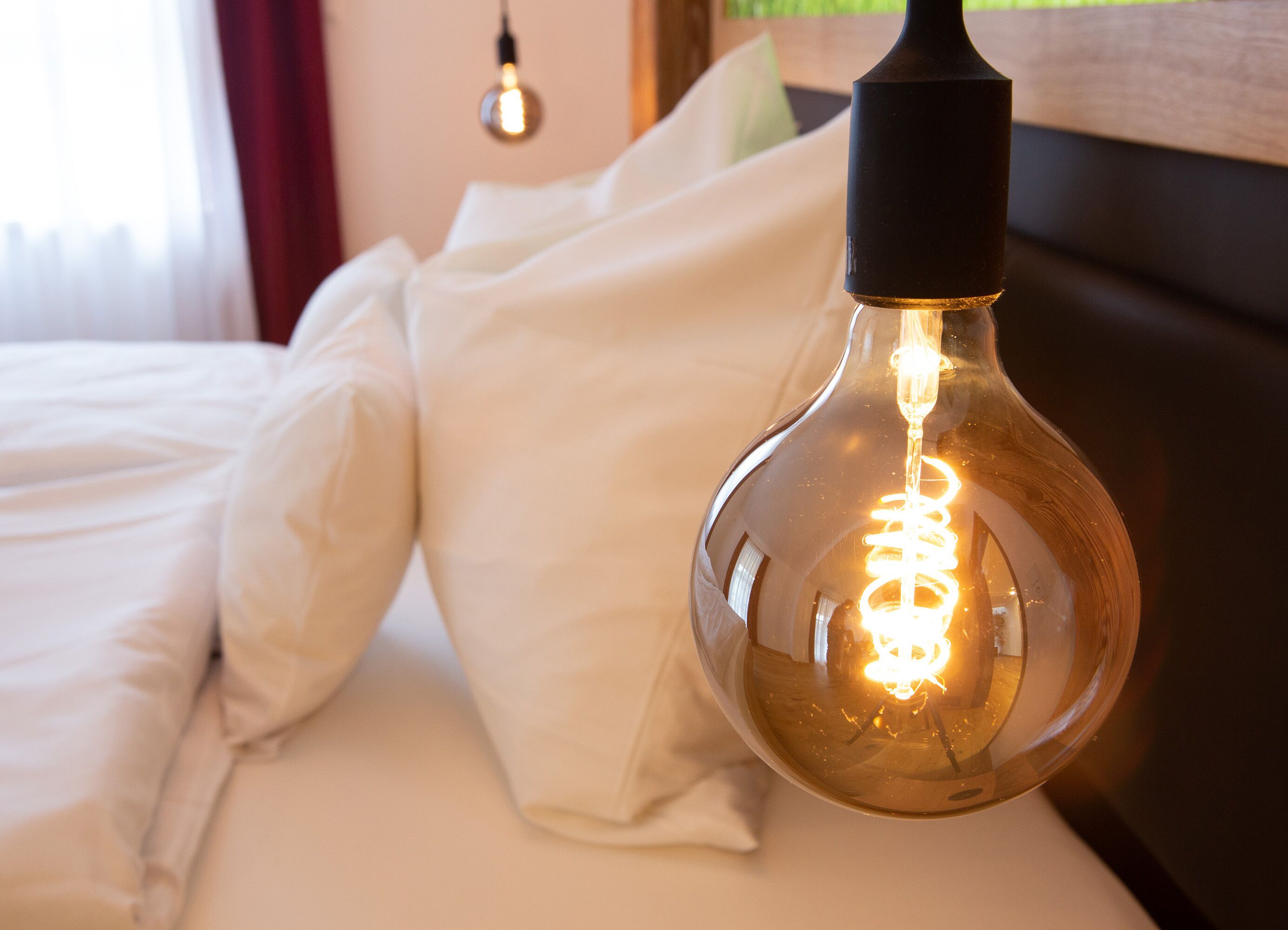 Una cama con ropa de cama blanca y una bombilla colgante.