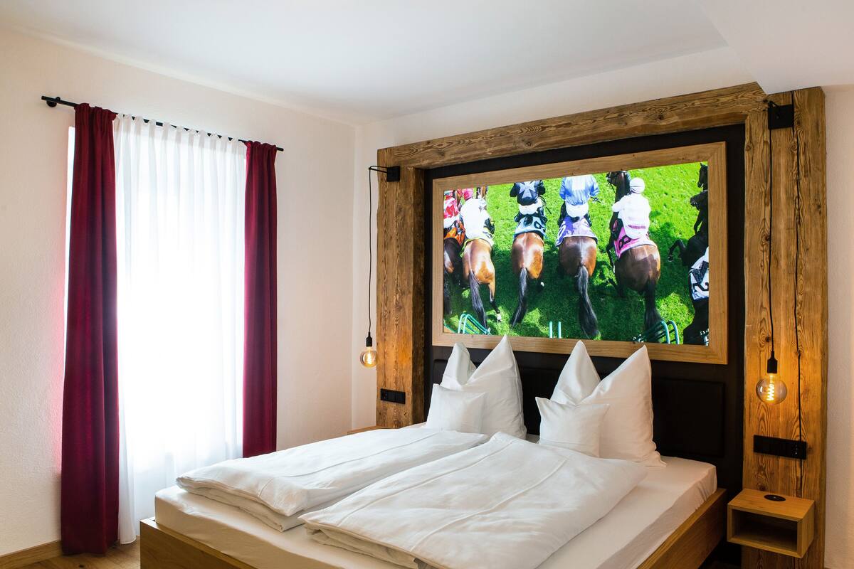 Une chambre d’hôtel avec un lit, un téléviseur fixé au mur en bois et une petite table de chevet en bois.
