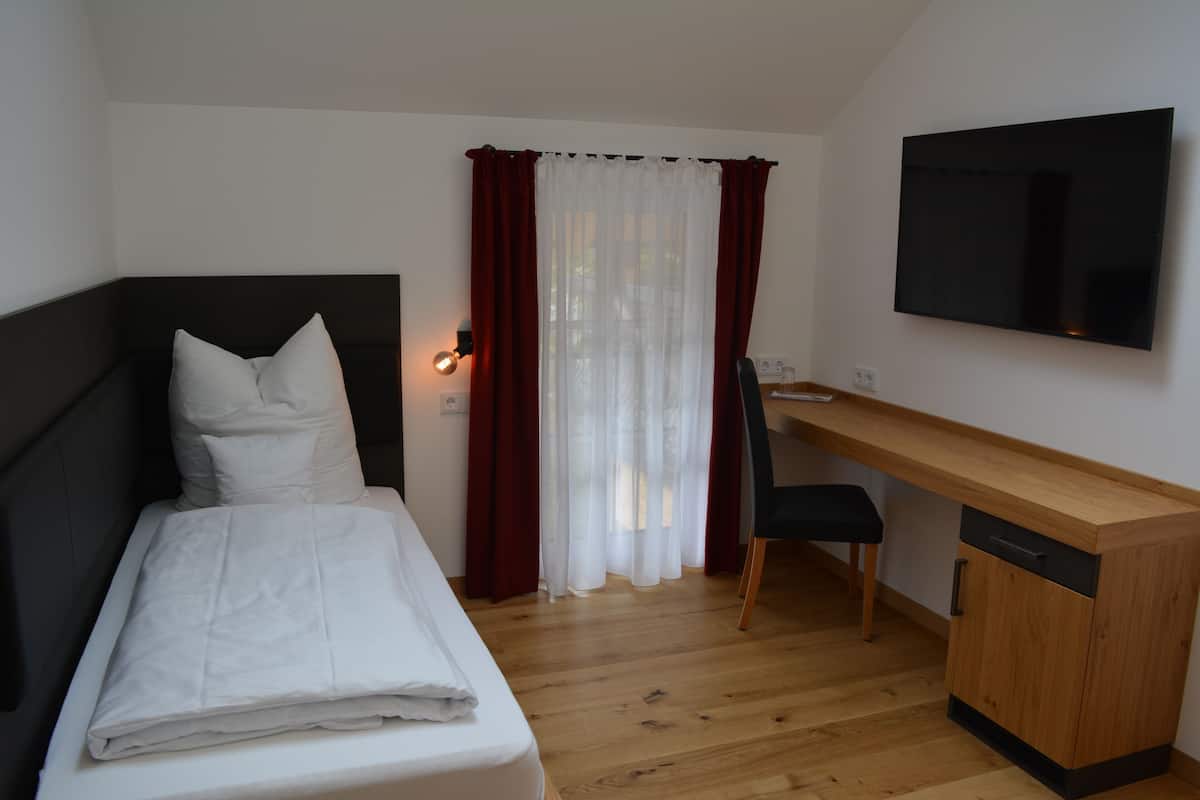 Une chambre à coucher avec un lit, un bureau, une chaise, un téléviseur et une fenêtre avec des rideaux.
