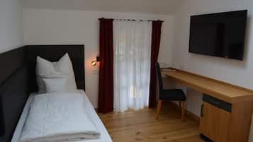 A bedroom with a bed, a desk, a chair, a TV, and a window with curtains.