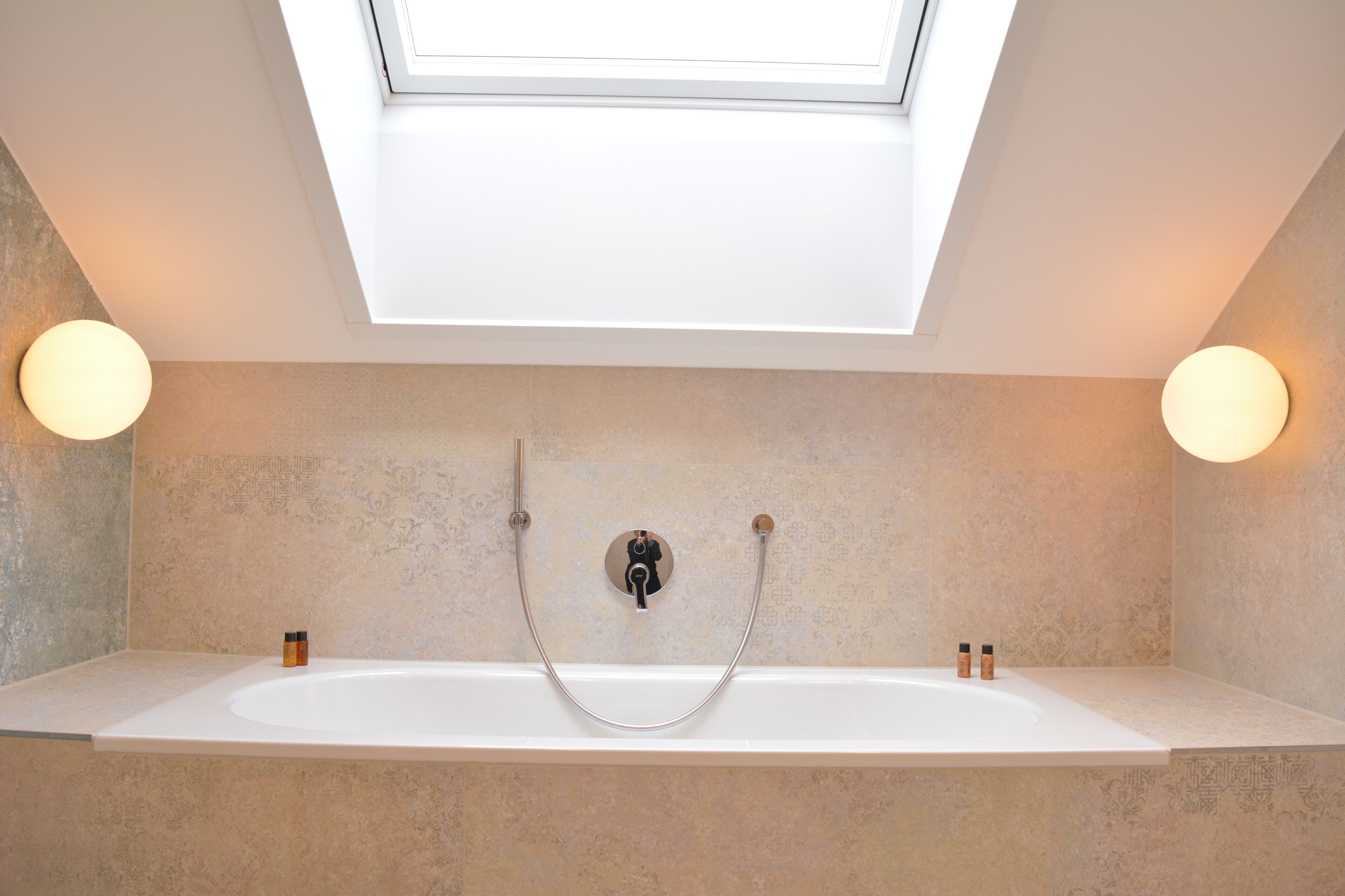 A modern bathroom with a skylight, a freestanding bathtub, and two wall-mounted lights.