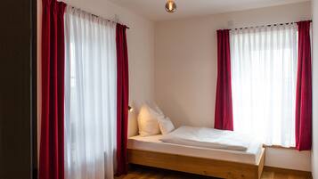 Ein Schlafzimmer mit einem hölzernen Bett, weißer Bettwäsche, roten Vorhängen und einer modernen Leuchte.