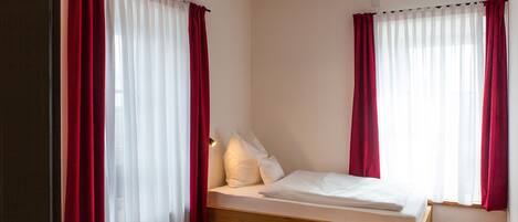 Een slaapkamer met een houten bed, witte beddengoed, rode gordijnen en een moderne lamp.