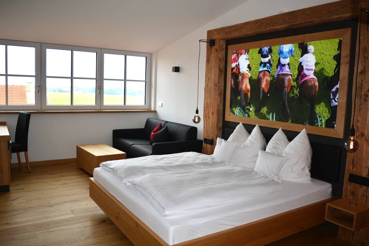 Une chambre avec un grand lit, une tête de lit en bois, un téléviseur fixé au mur, un bureau et une chaise.