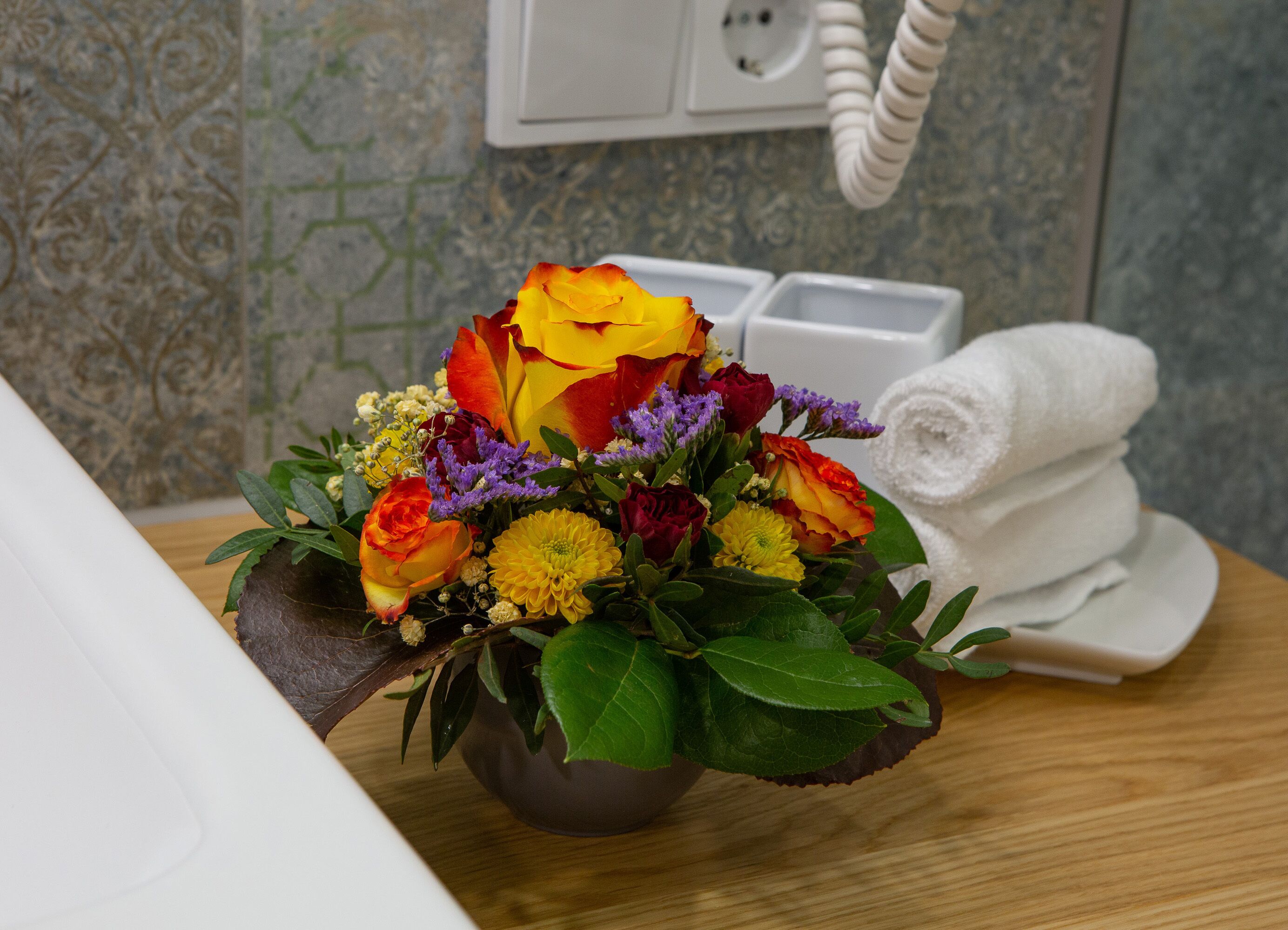 A bathroom with a wooden vanity, a white towel, and a floral arrangement on the counter.