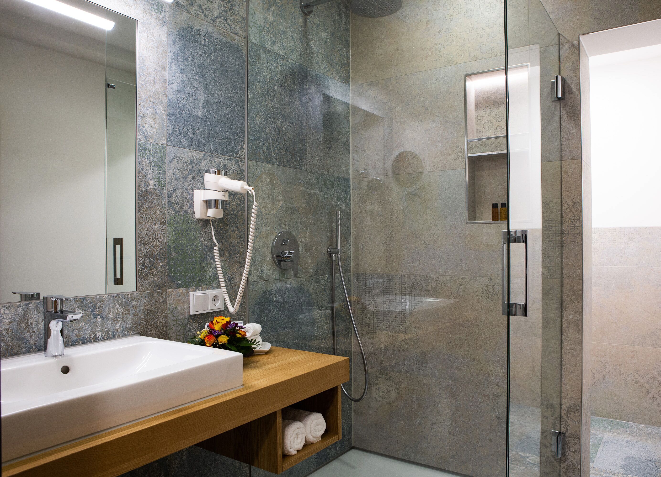 A modern bathroom with a large mirror, a sink, a shower, and a wooden vanity.