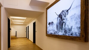 Un corridoio con pavimento in legno, un grande quadro con l'immagine di una mucca e porte che danno su diverse stanze.