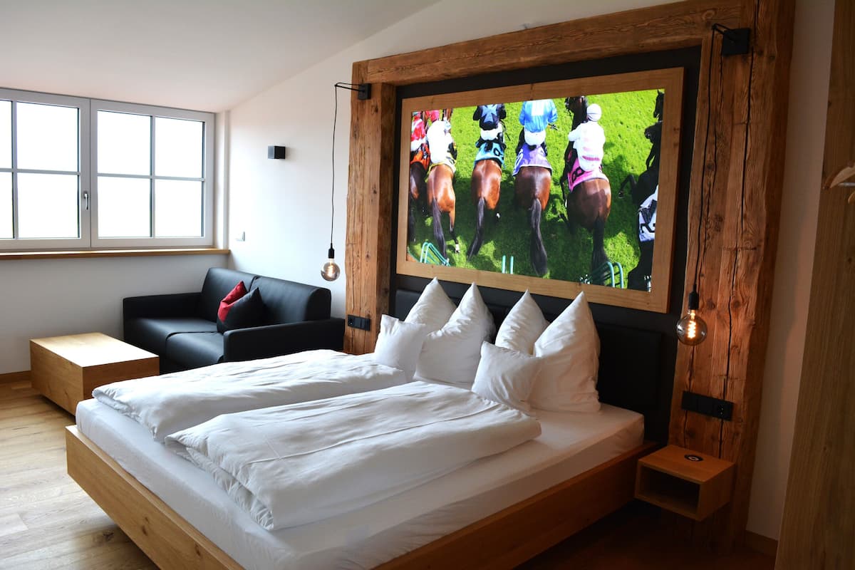 Une chambre à coucher moderne avec un grand lit, un téléviseur fixé au mur, une tête de lit en bois et une fenêtre équipée de stores.