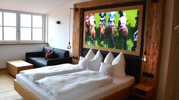 Une chambre à coucher moderne avec un grand lit, un téléviseur fixé au mur, une tête de lit en bois et une fenêtre équipée de stores.