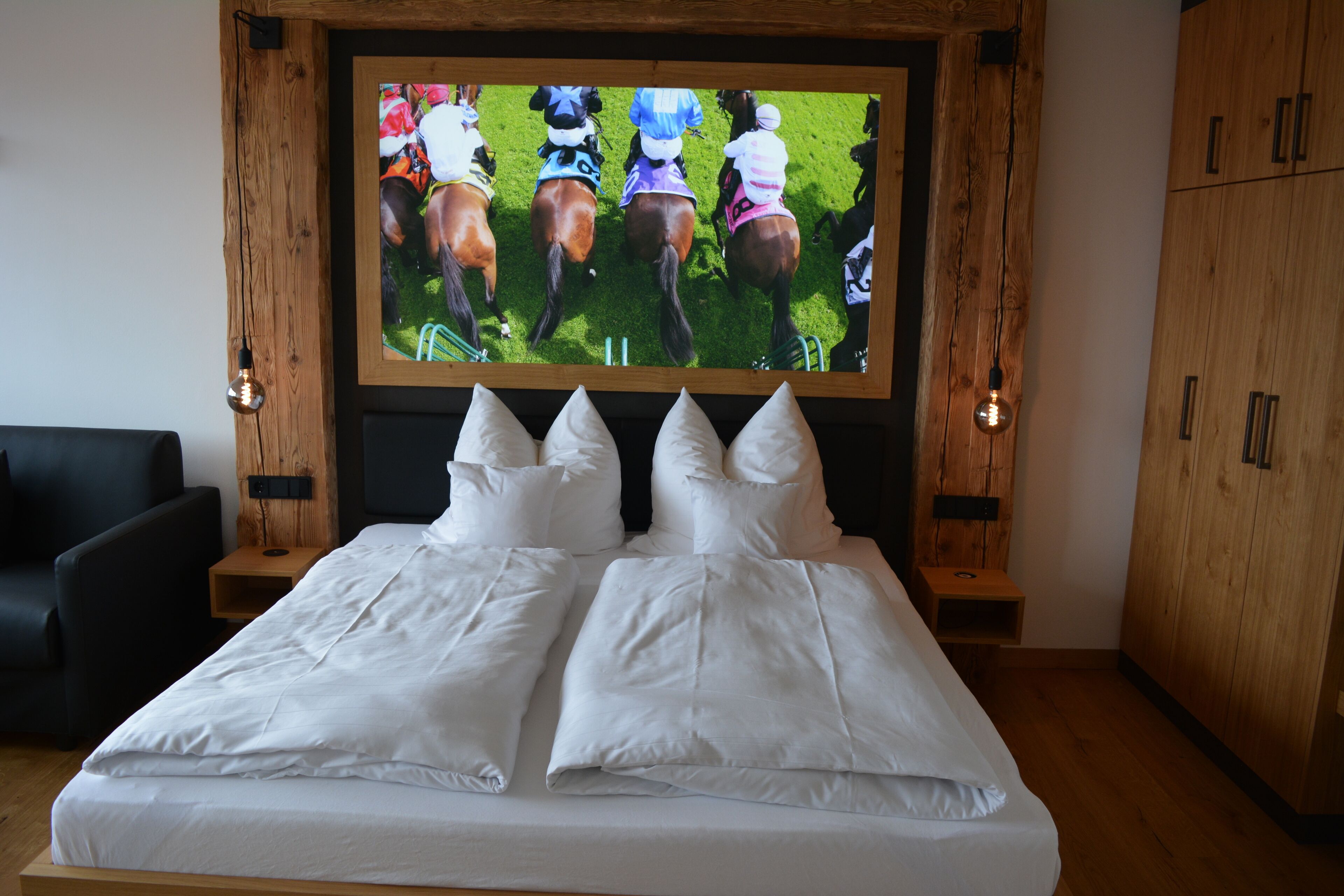 Un dormitorio con una cama grande, televisor montado en la pared, muebles de madera y una silla negra.