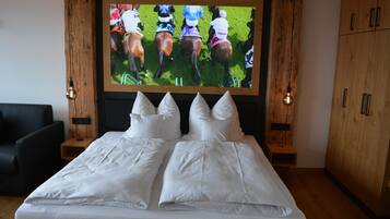 Un dormitorio con una cama grande, televisor montado en la pared, muebles de madera y una silla negra.