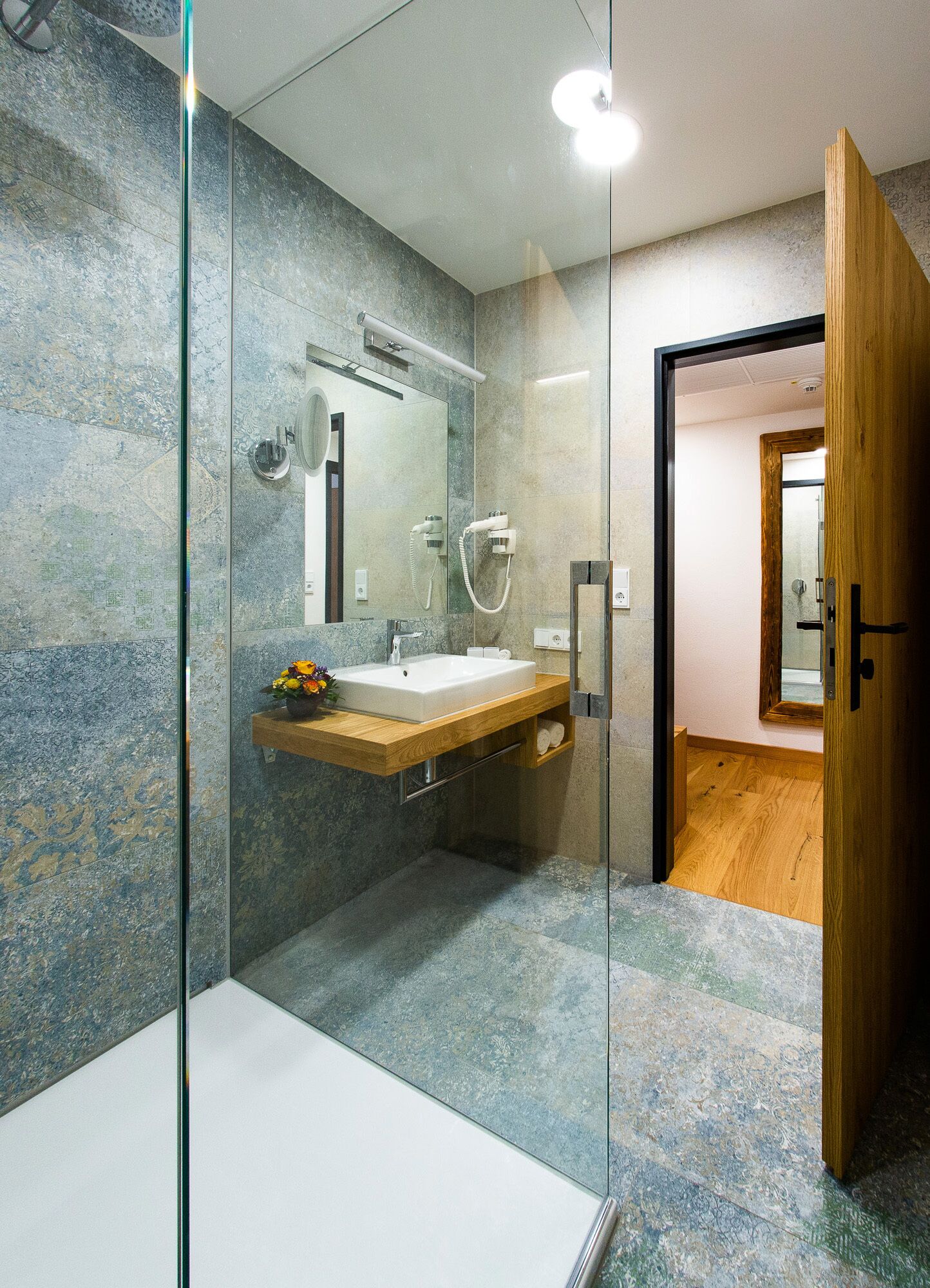 Een moderne badkamer met een glazen douchecabine, een houten wastafelmeubel en een grote spiegel.