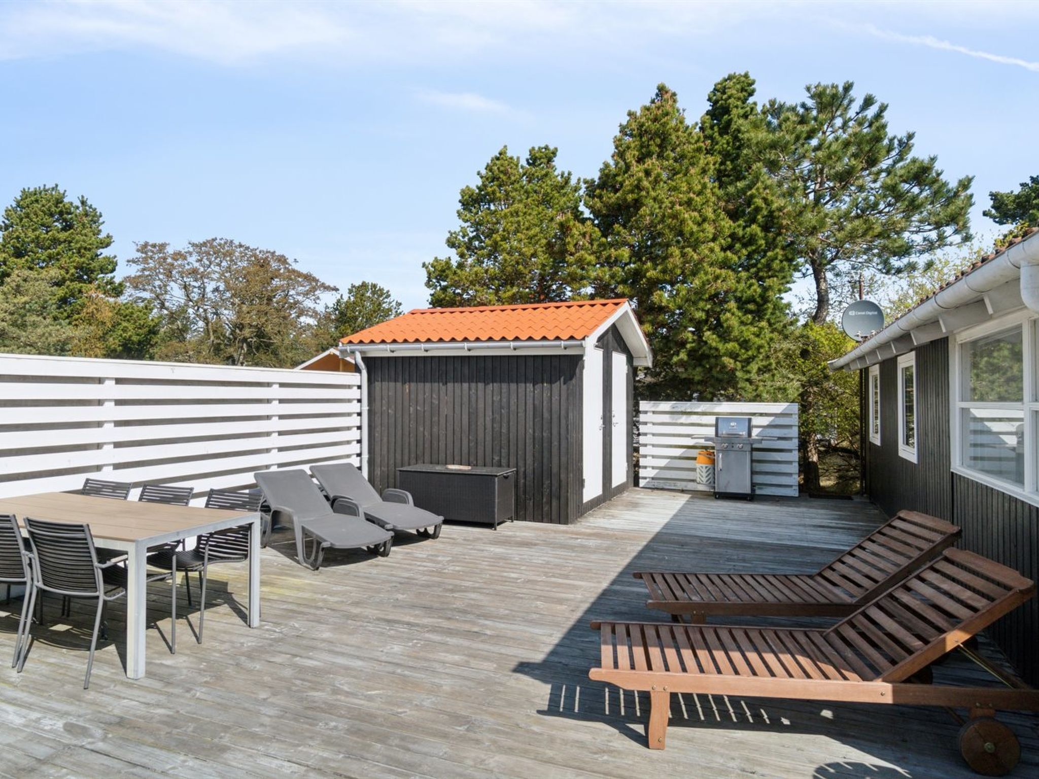 Una terraza con sillones de descanso, una mesa y zona de barbacoa.