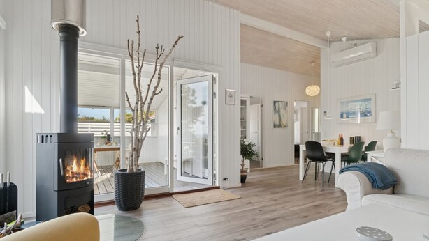 A modern living room with a wood-burning stove, a sofa, a dining area, and a kitchen visible through an open door.
