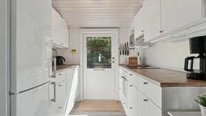 A narrow kitchen with white cabinets, a wooden countertop, and a door leading to a balcony.