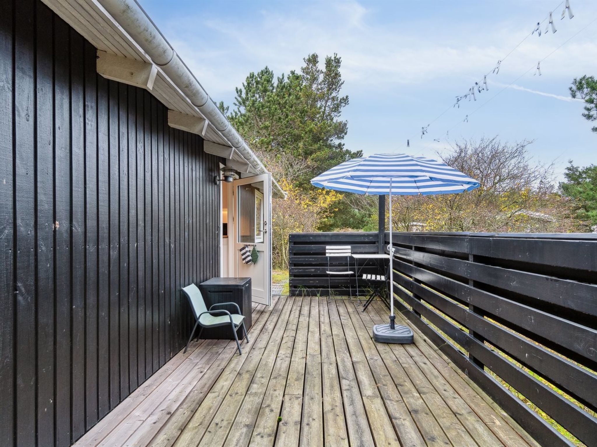 A wooden deck with a black railing, a striped umbrella, and a chair.