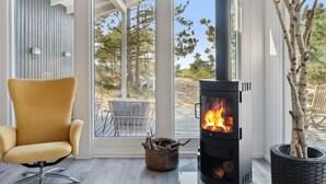 A modern interior with a large glass door leading to an outdoor patio, a black wood-burning stove, a yellow chair, and a potted tree.