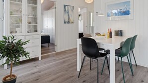 A modern kitchen with white cabinetry, a dining area with a white table and green chairs, and a potted plant.