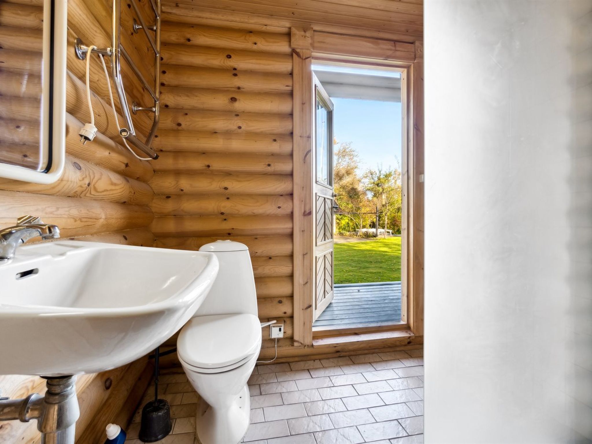Une salle de bain rustique, aménagée dans une cabane en bois, avec un lavabo, des toilettes et une porte donnant sur une terrasse.