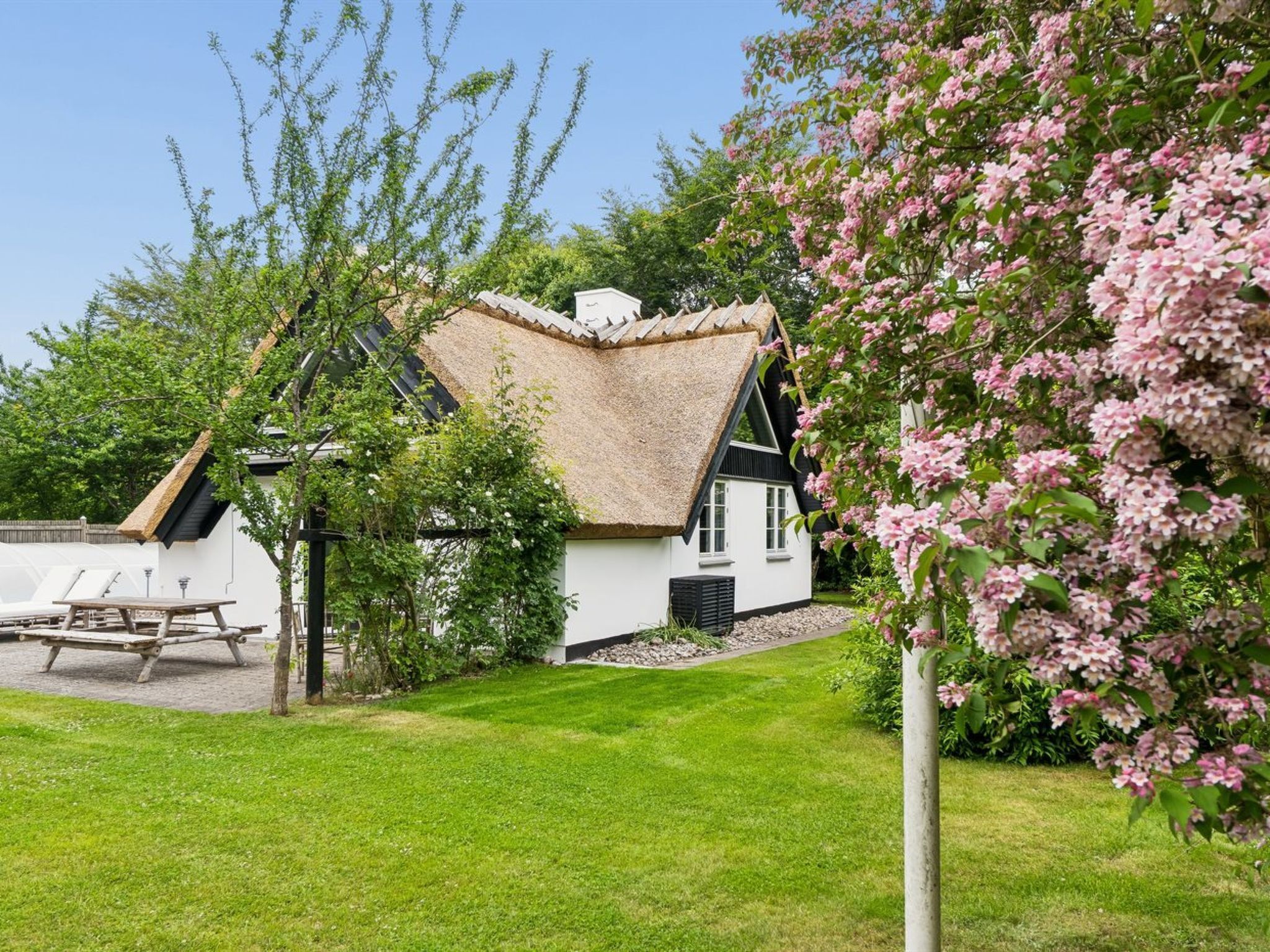 Ein traditionelles Haus mit Strohdach, einem gepflegten Rasen und blühenden Blumen.