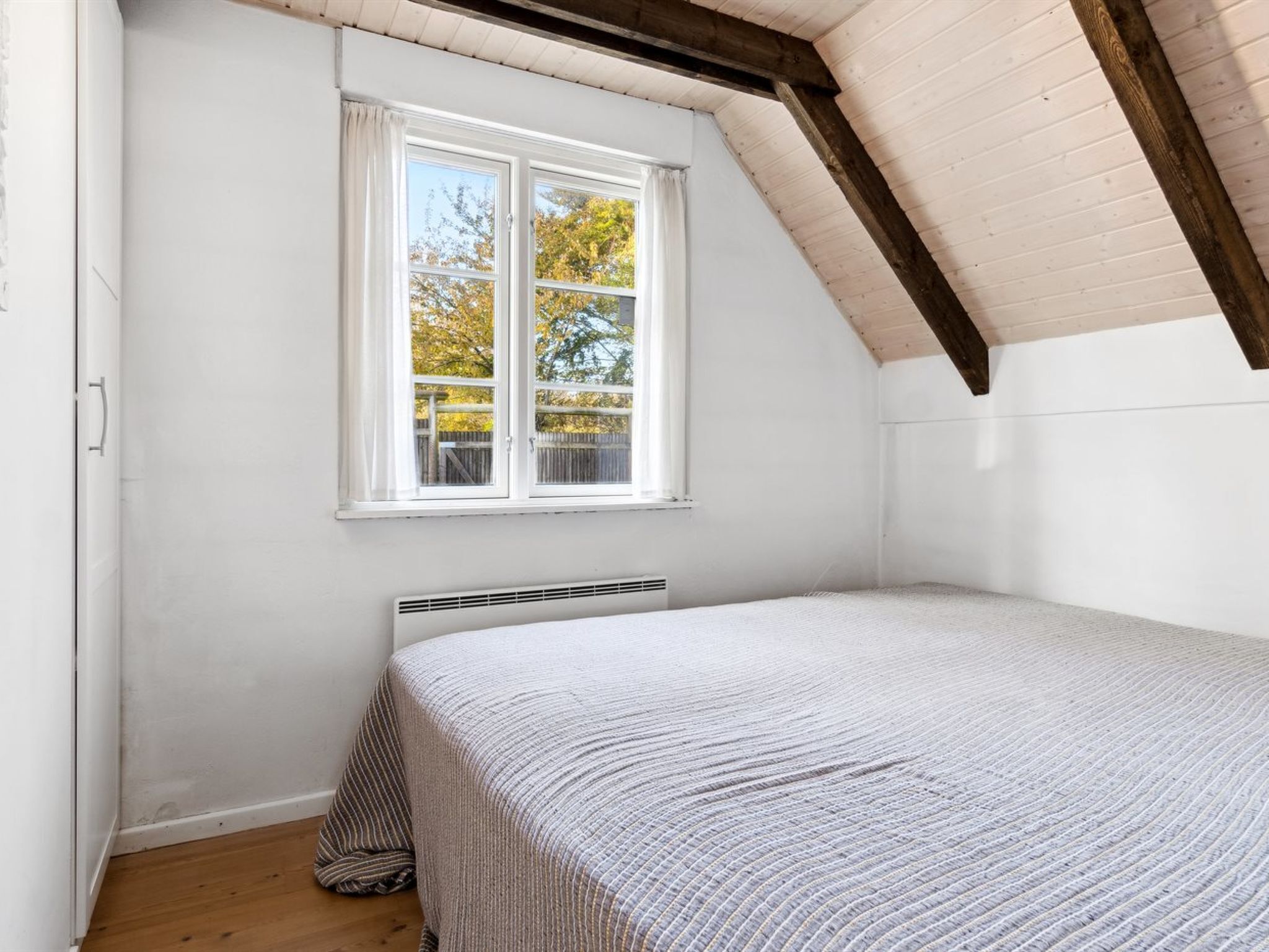 A bedroom with a sloped ceiling, a window with a view of trees, and a radiator below the window.