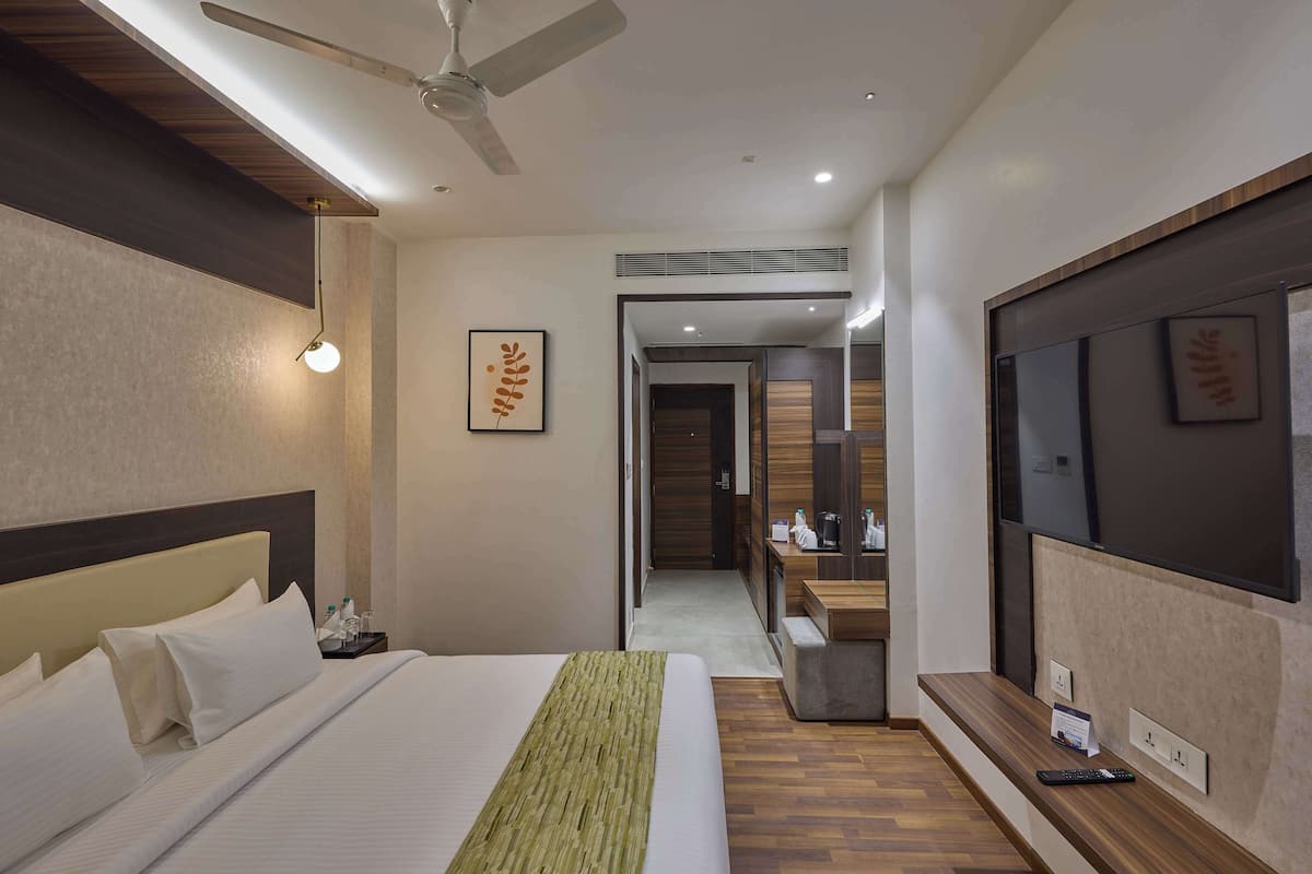 A hotel room with a large bed, a ceiling fan, a TV, a bedside table, and a mirror.