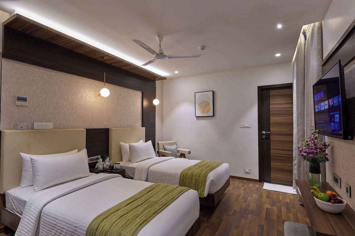 A hotel room with two beds, a ceiling fan, a flat-screen TV, a wooden floor, and a small table with fruit.