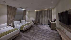 Een hotelkamer met twee bedden, een bureau, een stoel, een televisie en een plafondventilator.