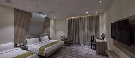A hotel room with two beds, a desk, a chair, a TV, and a ceiling fan.