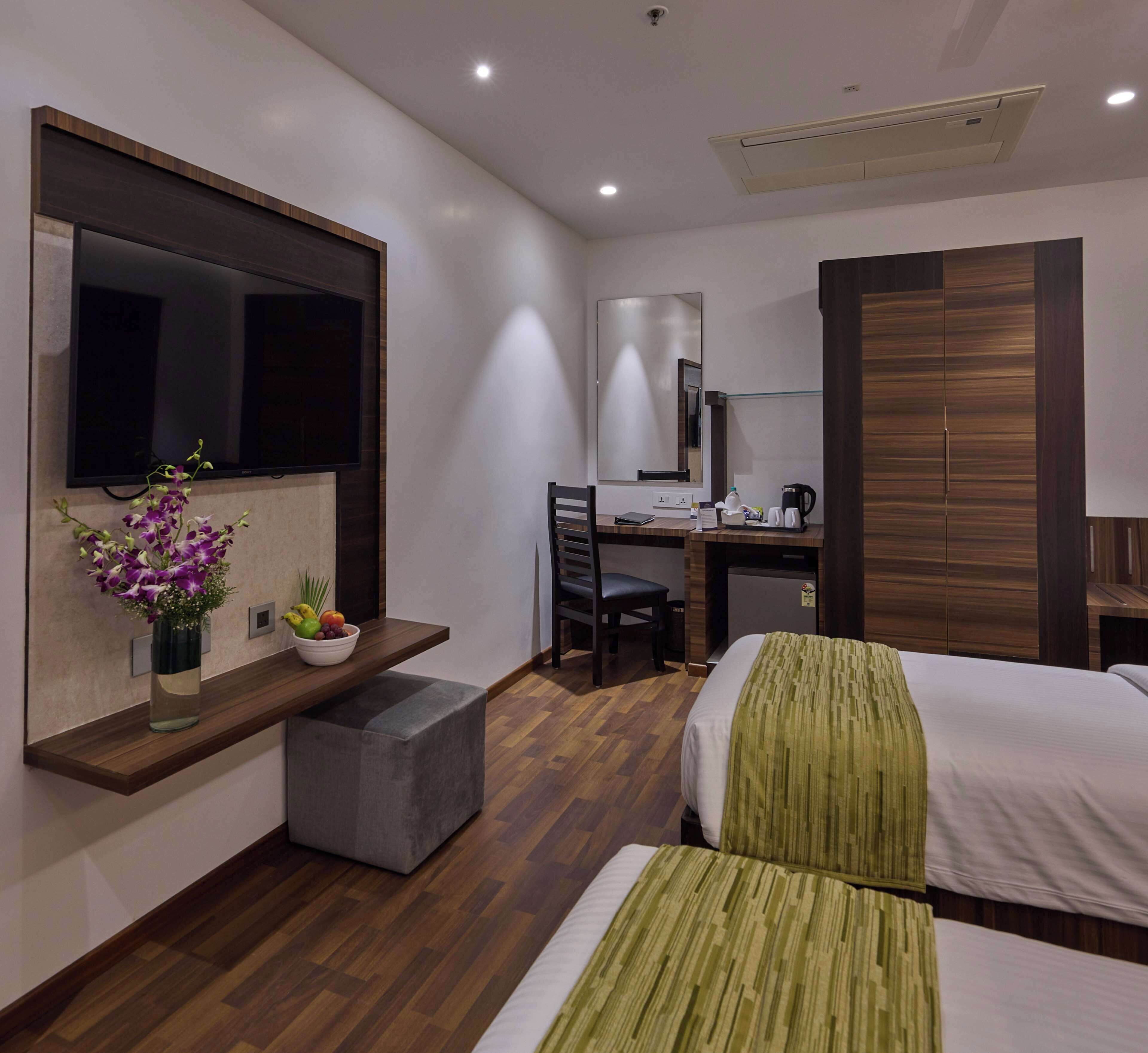 Una habitación de hotel moderna con una cama, un escritorio, una silla, un televisor y una mesita con un florero.