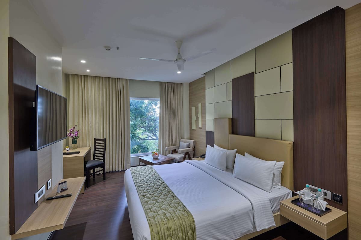 A hotel room with a bed, desk, chair, TV, and a window with curtains.