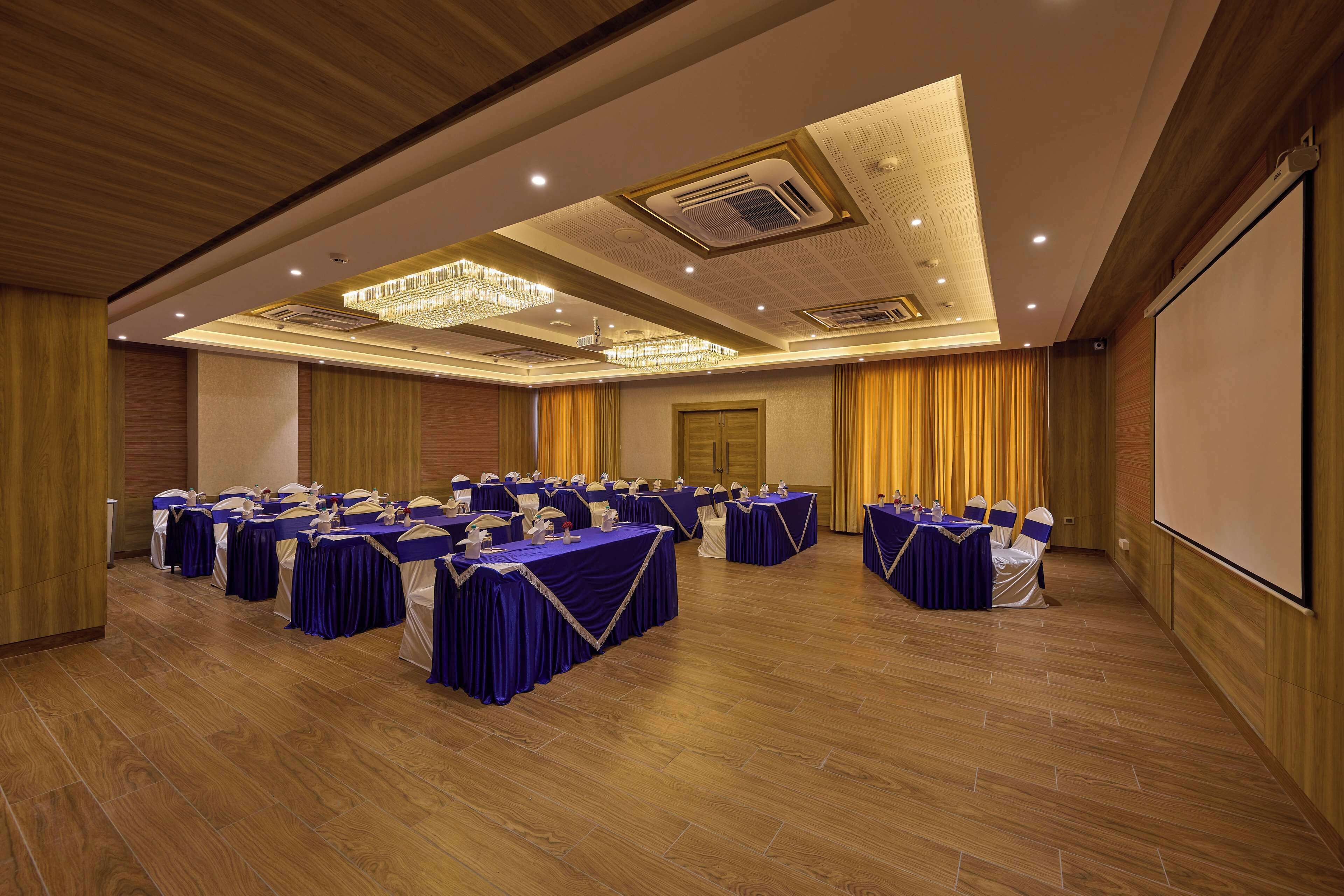 Un salón de conferencias con varias mesas, sillas y una pantalla para proyector.