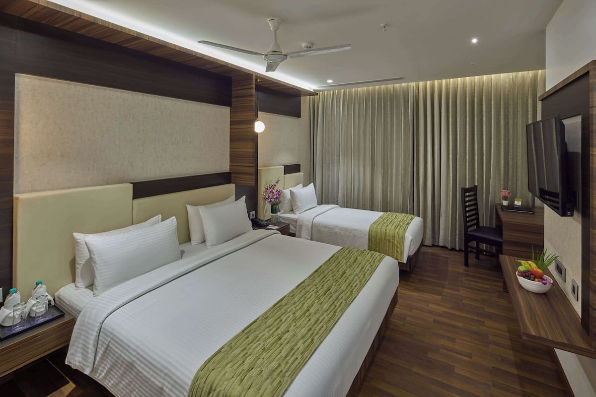 A hotel room with two beds, a ceiling fan, a TV, and a small table with a bowl of fruit.