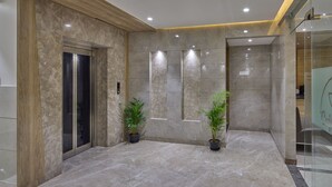 Een moderne lobby met een marmeren vloer, houten details en twee potplanten.