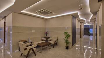 A modern lobby with a seating area, a potted plant, and a staircase in the background.