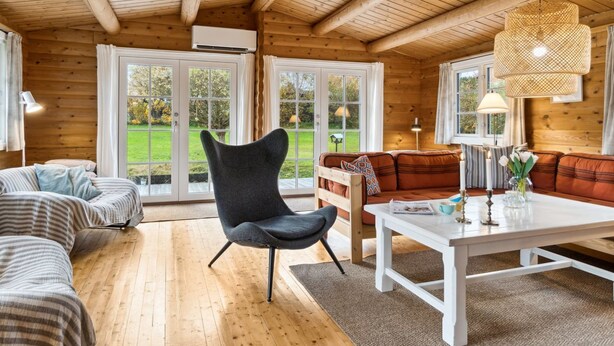 Ein gemütliches Blockhaus-Interieur mit Holzbalkendecke, einer Couch, einem Sessel und einem Esstisch.
