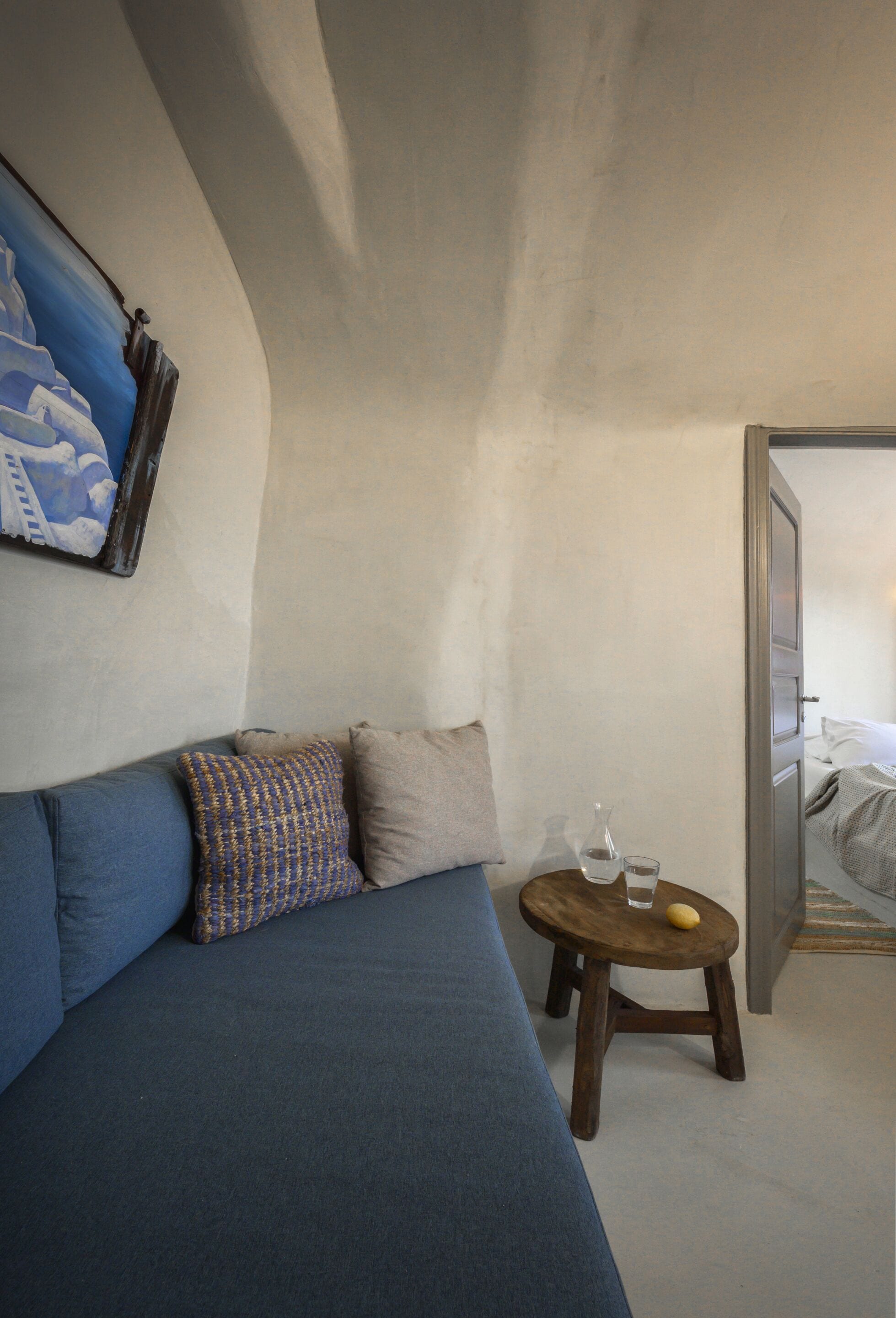 A room with a blue sofa, a small wooden table with a glass and a lemon, and a painting on the wall.