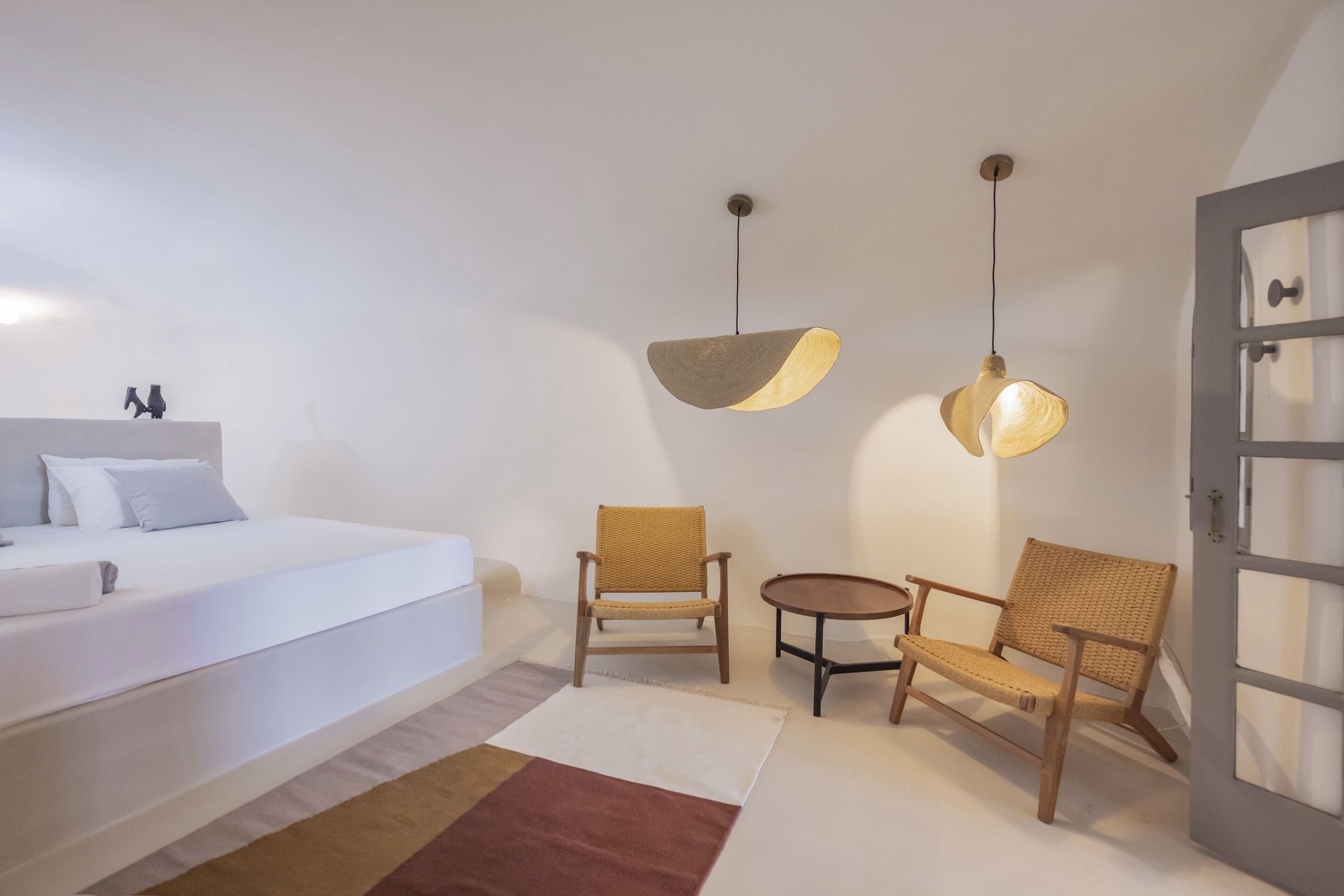 A bedroom with a bed, two chairs, a small table, and two pendant lights.