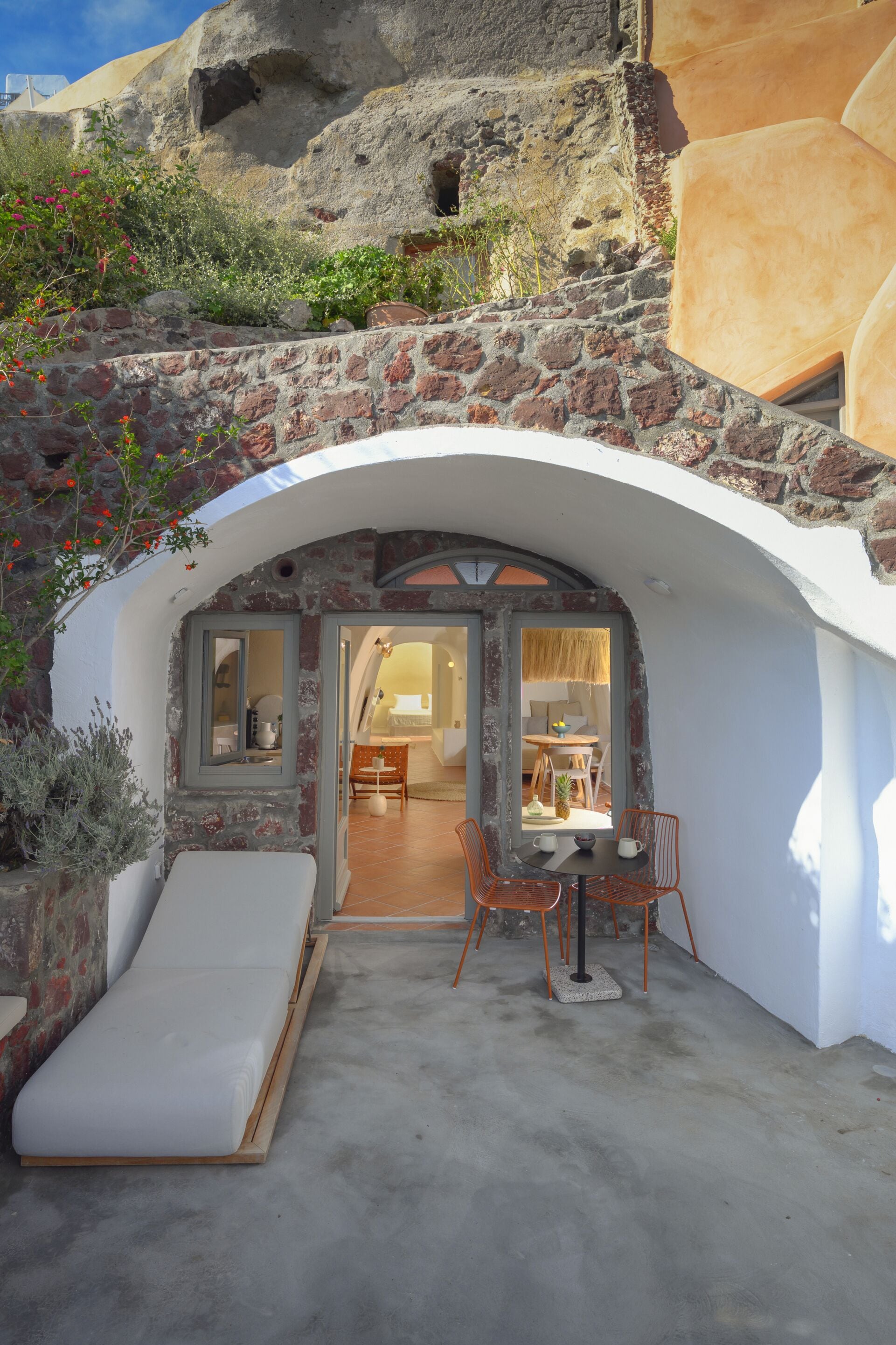 A stone house with an arched entrance, a patio with a table and chairs, and a view of the surrounding landscape.